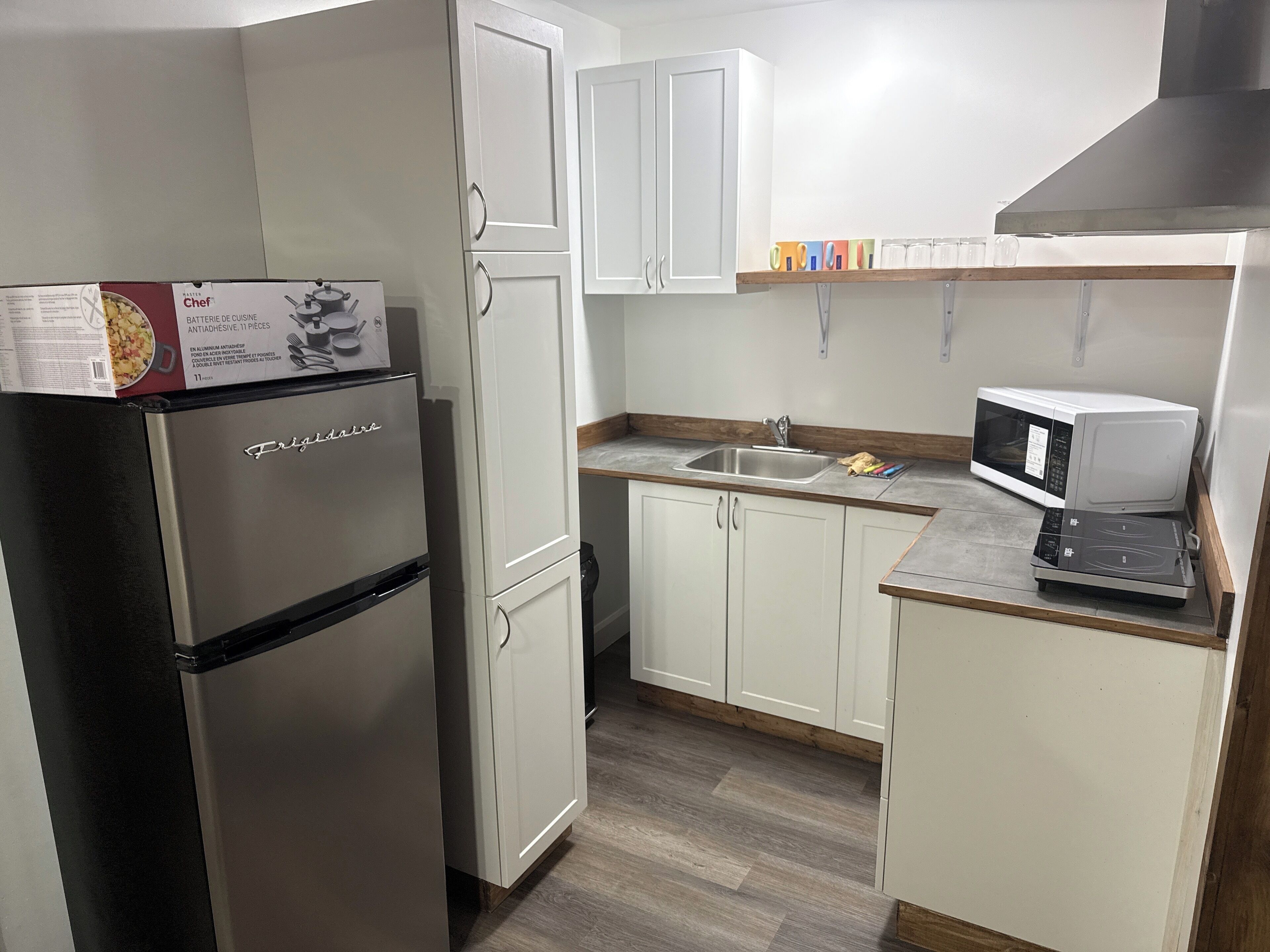 A compact kitchen with white cabinets, a stainless steel refrigerator, a microwave, and a sink.