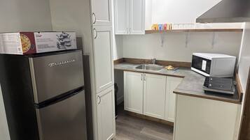A compact kitchen with white cabinets, a stainless steel refrigerator, a microwave, and a sink.