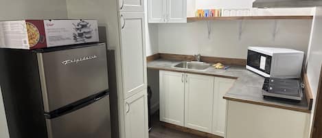 A compact kitchen with white cabinets, a stainless steel refrigerator, a microwave, and a sink.