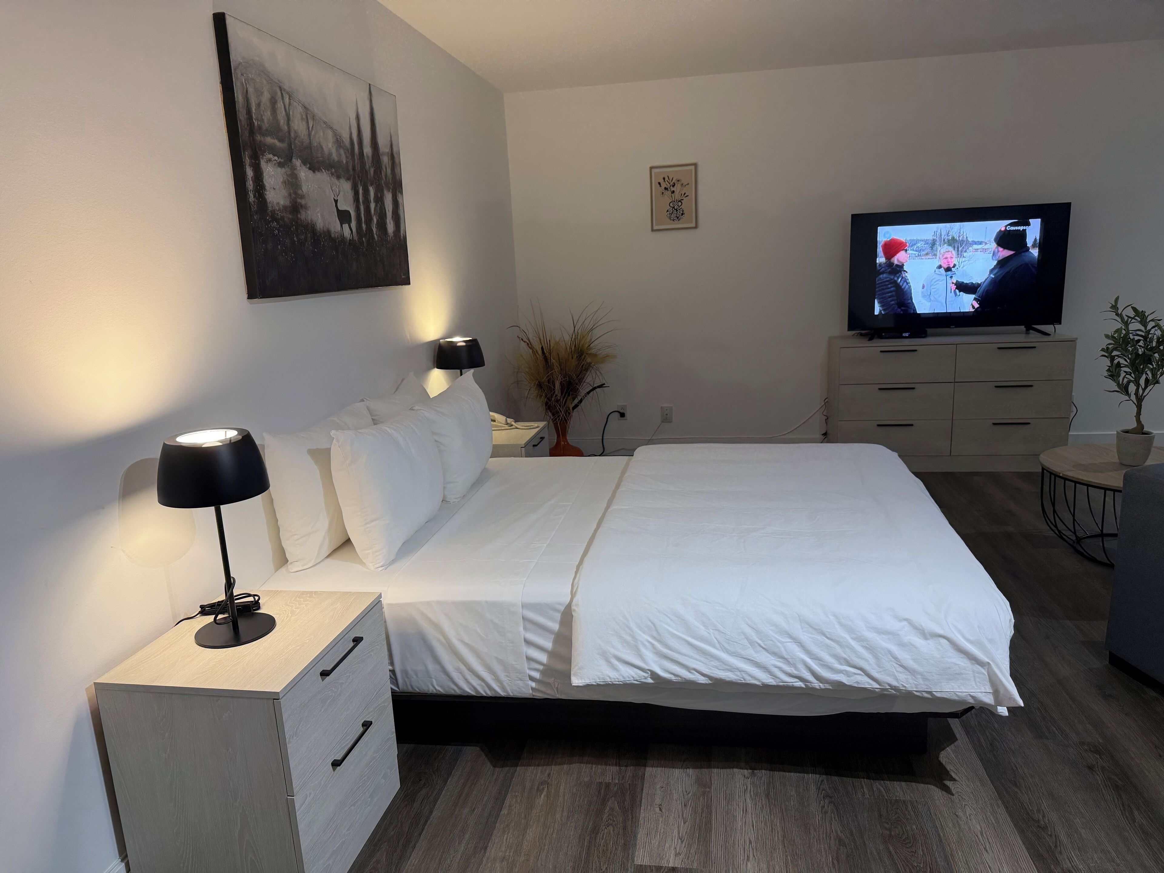 A modern hotel room with a large bed, bedside lamps, a television, and a small side table.