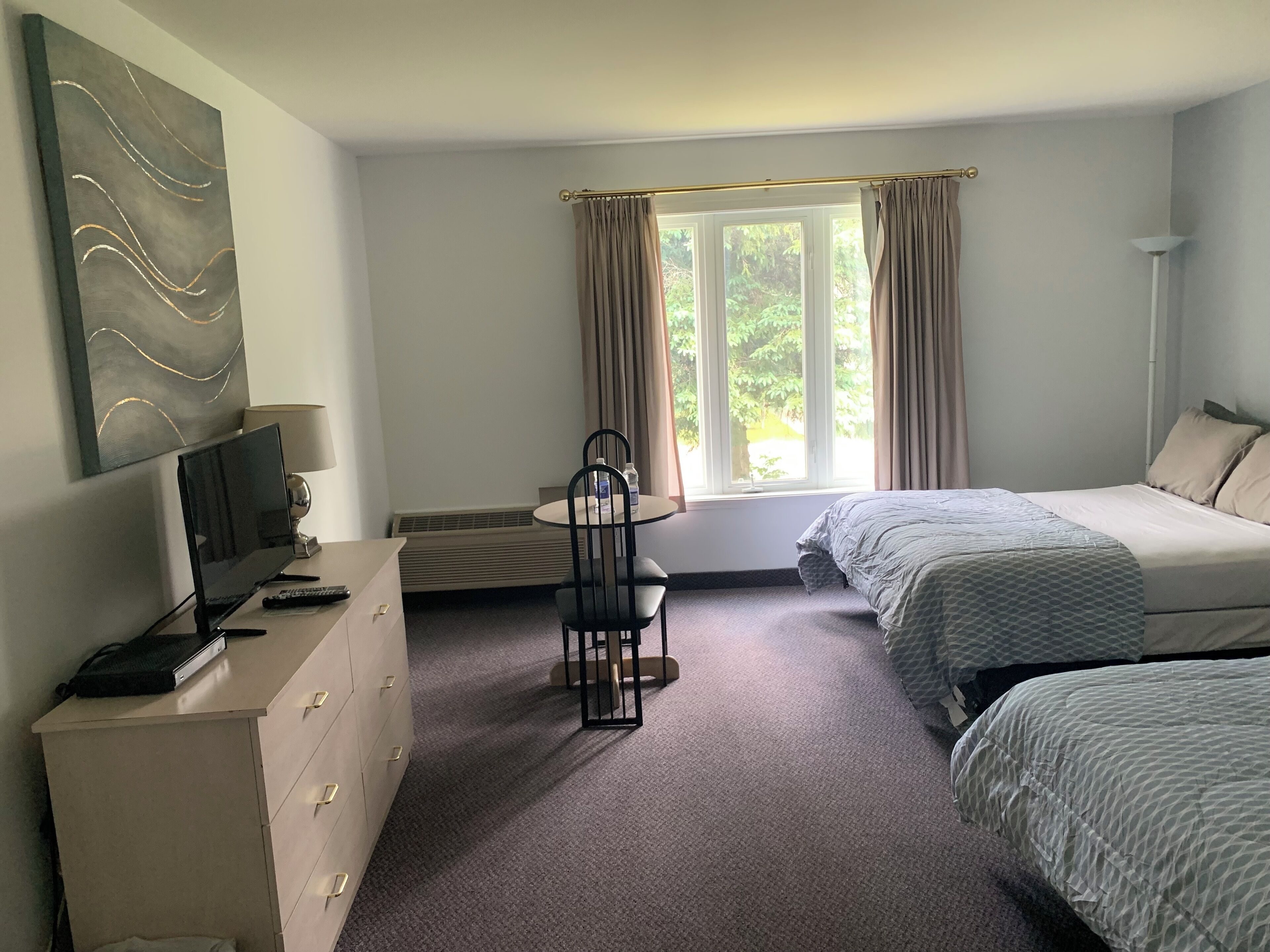 A hotel room with a bed, a desk with a chair, a TV, and a window with curtains.