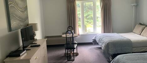 A hotel room with a bed, a desk with a chair, a TV, and a window with curtains.