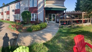 A two-story building with a reception area, a covered outdoor seating area, and a small garden with a tree and shrubs. - Hôtel saint-côme (Saint-Côme)
