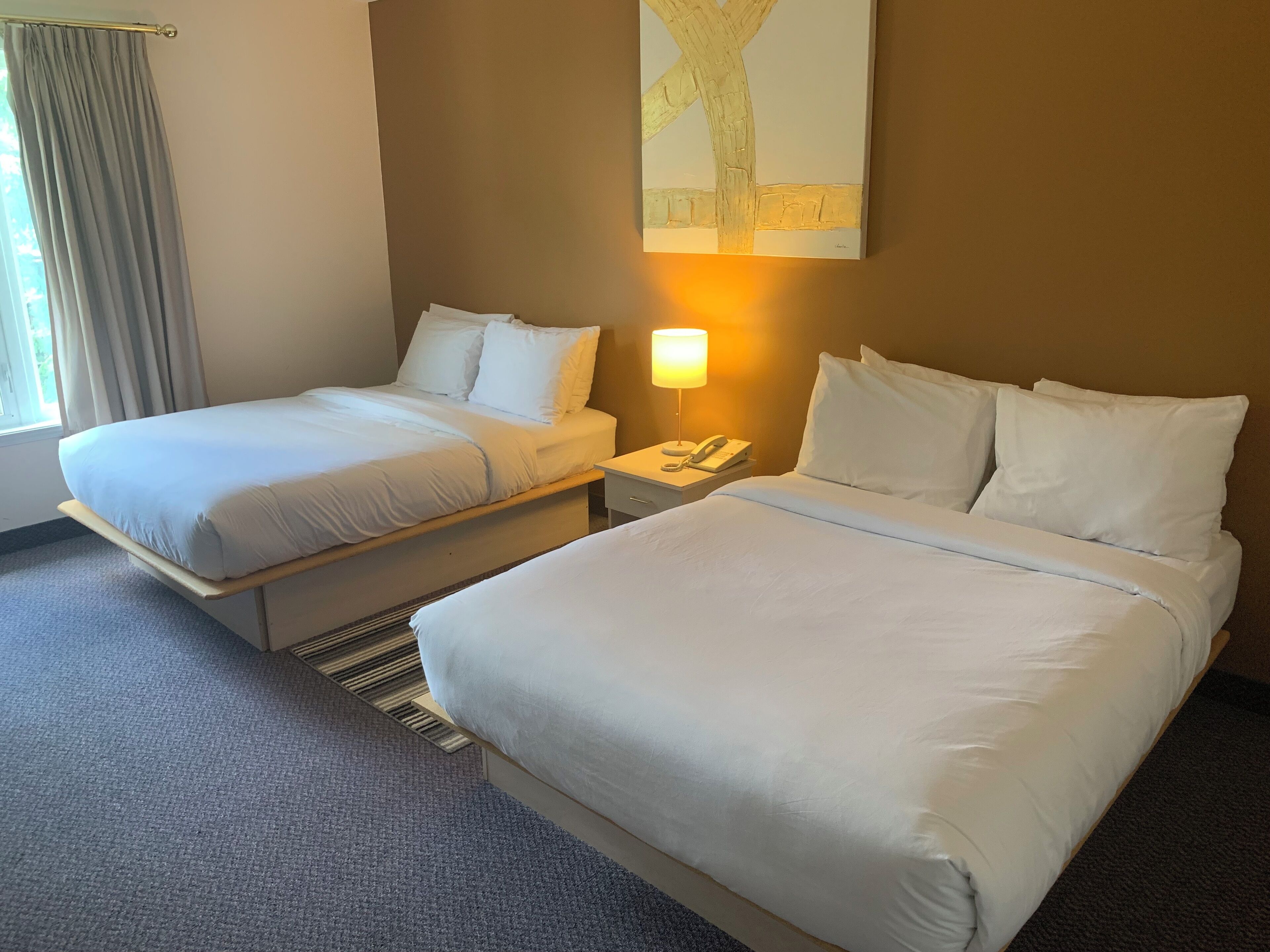 A hotel room with two beds, a bedside table with a lamp, and a painting on the wall.
