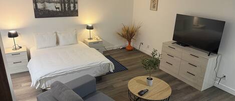 Un dormitorio moderno con una cama grande, mesitas de noche con lámparas, un televisor, un sofá y una pequeña mesa redonda.