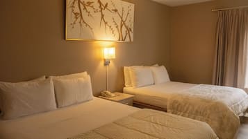 A hotel room with two beds, a nightstand with a phone, a wall-mounted lamp, and a large framed artwork above the beds.