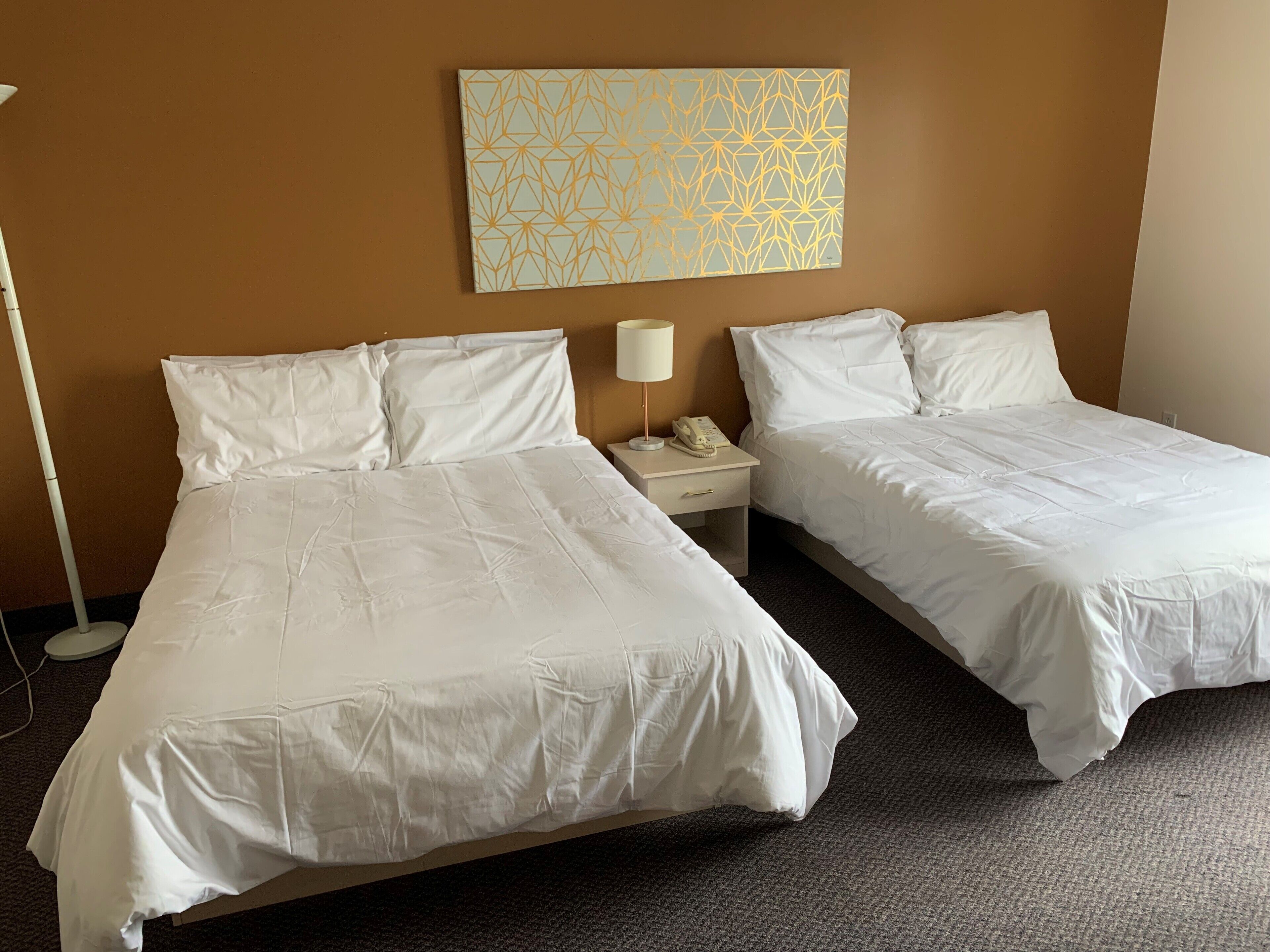 A hotel room with two single beds, a nightstand with a lamp and phone, and a wall art piece.