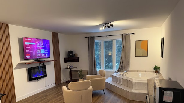 A modern hotel room with a TV, seating area, and a bathtub. - Hôtel saint-côme (Saint-Côme)