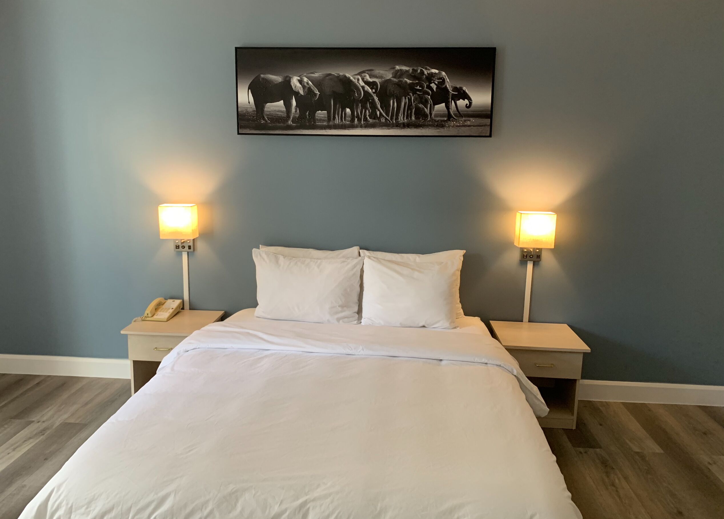 Un dormitorio con una cama, dos mesitas de noche, un teléfono y un cuadro en la pared.