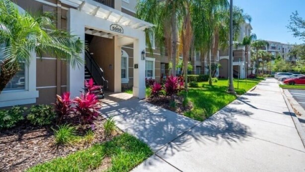 A modern apartment building with a number '5000' sign, a covered entrance, and a well-maintained garden with palm trees and shrubs. - Exclusive apartment at Vista Cay Resort (Orlando)