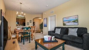 A living room with a dark grey sofa, a wooden coffee table, and a dining area with wooden chairs and a table. - Exclusive apartment at Vista Cay Resort (Orlando)