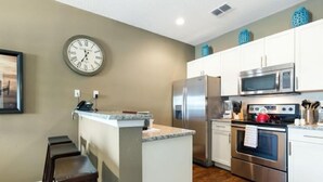 Een moderne keuken met een centraal eiland, roestvrijstalen apparatuur en een klok aan de muur.
