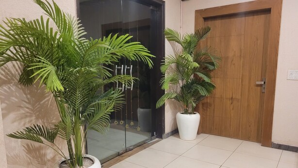 A hallway with potted plants, a glass door, and a wooden door. - The Aura Grand (Rohtak)