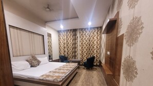 A hotel room with a large bed, a small table, two chairs, a mirror, and patterned curtains. - The Aura Grand (Rohtak)