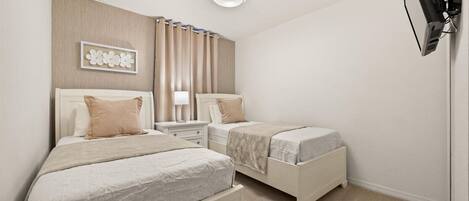 A hotel room with two beds, a bedside table with a lamp, a ceiling light, and a TV mounted on the wall.