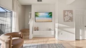 A modern living room with a flat-screen TV on a white console, a beige armchair, and a patterned rug. - Cozy 3BR house affordable at Bella Vida Resort (Kissimmee)