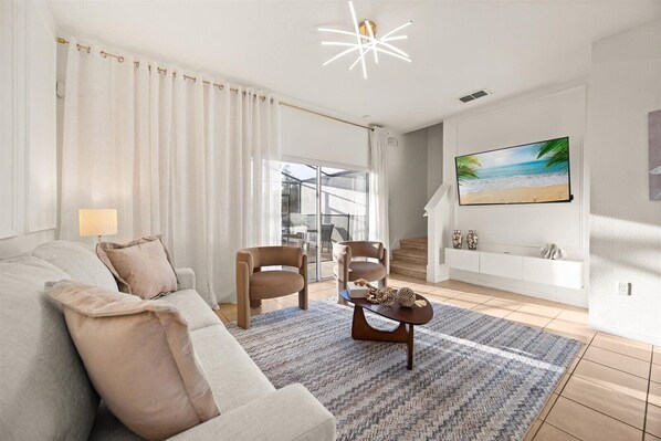 A modern living room with a sofa, chairs, a coffee table, and a TV on the wall.