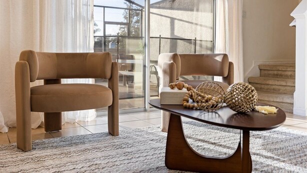 A modern living room with two brown leather chairs, a dark wooden coffee table, and a glass door leading outside. - Cozy 3BR house affordable at Bella Vida Resort (Kissimmee)