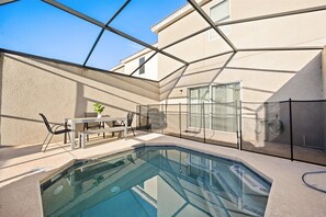 A swimming pool with a glass enclosure, a table with chairs, and a potted plant.