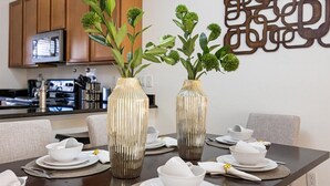 A dining table set with white plates, bowls, and silverware, flanked by two decorative vases with green foliage. - Cozy 3BR house affordable at Bella Vida Resort (Kissimmee)