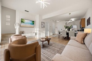 A spacious living area with a large flat-screen TV, a sofa, and a dining area with chairs and a table.