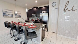 A modern kitchen with dark cabinets, stainless steel appliances, and a central island with bar stools. - Beautiful 4BR Storey Lake Resort close to Disney (Kissimmee)