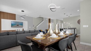 Un espace de repas moderne avec une table en bois pouvant accueillir six personnes, des canapés gris et des luminaires contemporains.