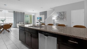 A modern kitchen with a central island, dark cabinetry, and a dining area with chairs and a table. - Comfortable 5BR Home Near Disney 10 min (Kissimmee)