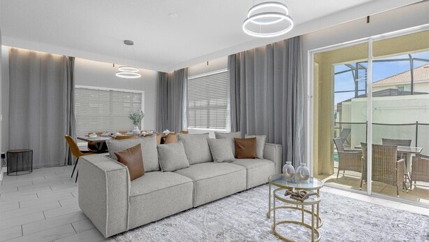 A modern living room with a grey sofa, a glass coffee table, and a dining area with a table and chairs. - Comfortable 5BR Home Near Disney 10 min (Kissimmee)