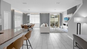 A modern kitchen with a marble countertop, a dining area with chairs, a sofa, and a staircase leading to an upper level. - Comfortable 5BR Home Near Disney 10 min (Kissimmee)
