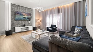 A modern living room with a marble wall, a flat-screen TV, a black leather sofa, a coffee table, and a large window with sheer curtains.