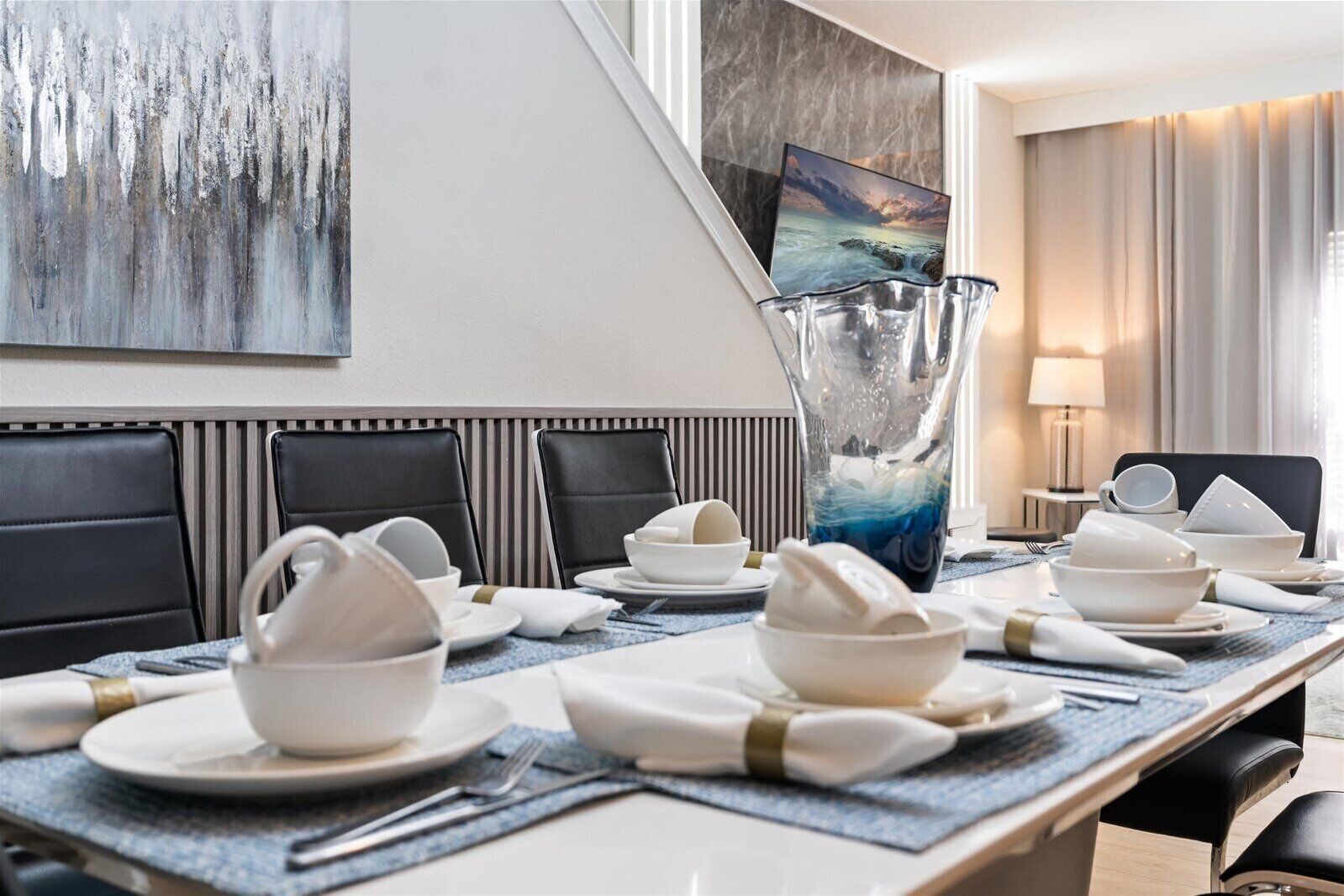 Ein Speisesaal eines Hotels mit einem langen Tisch, der für eine Mahlzeit gedeckt ist, schwarzen Polsterstühlen, einer großen Vase und einem Gemälde an der Wand.