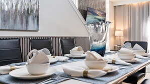 A hotel dining area with a long table set for a meal, black upholstered chairs, a large vase, and a painting on the wall.
