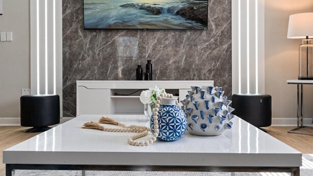 A modern living room with a marble wall, a flat-screen TV, a white console table, and decorative items.