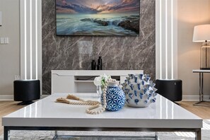 Una sala moderna con pared de mármol, televisor de pantalla plana, mesa consola blanca y elementos decorativos.