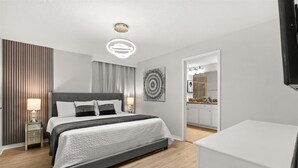 A modern hotel room with a large bed, bedside tables, a ceiling light, a wall-mounted artwork, and a view into the bathroom.