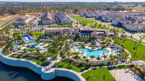 A residential area with a large swimming pool surrounded by houses, palm trees, and a landscaped garden. - Stylish 6BR Single Family at Solara Resort (Kissimmee)