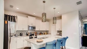 Une cuisine moderne avec des meubles blancs, un plan de travail en granit, un îlot central doté de tabourets et un éclairage suspendu.