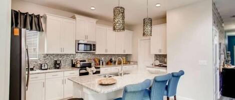 A modern kitchen with white cabinets, a granite countertop, a central island with bar stools, and pendant lighting.