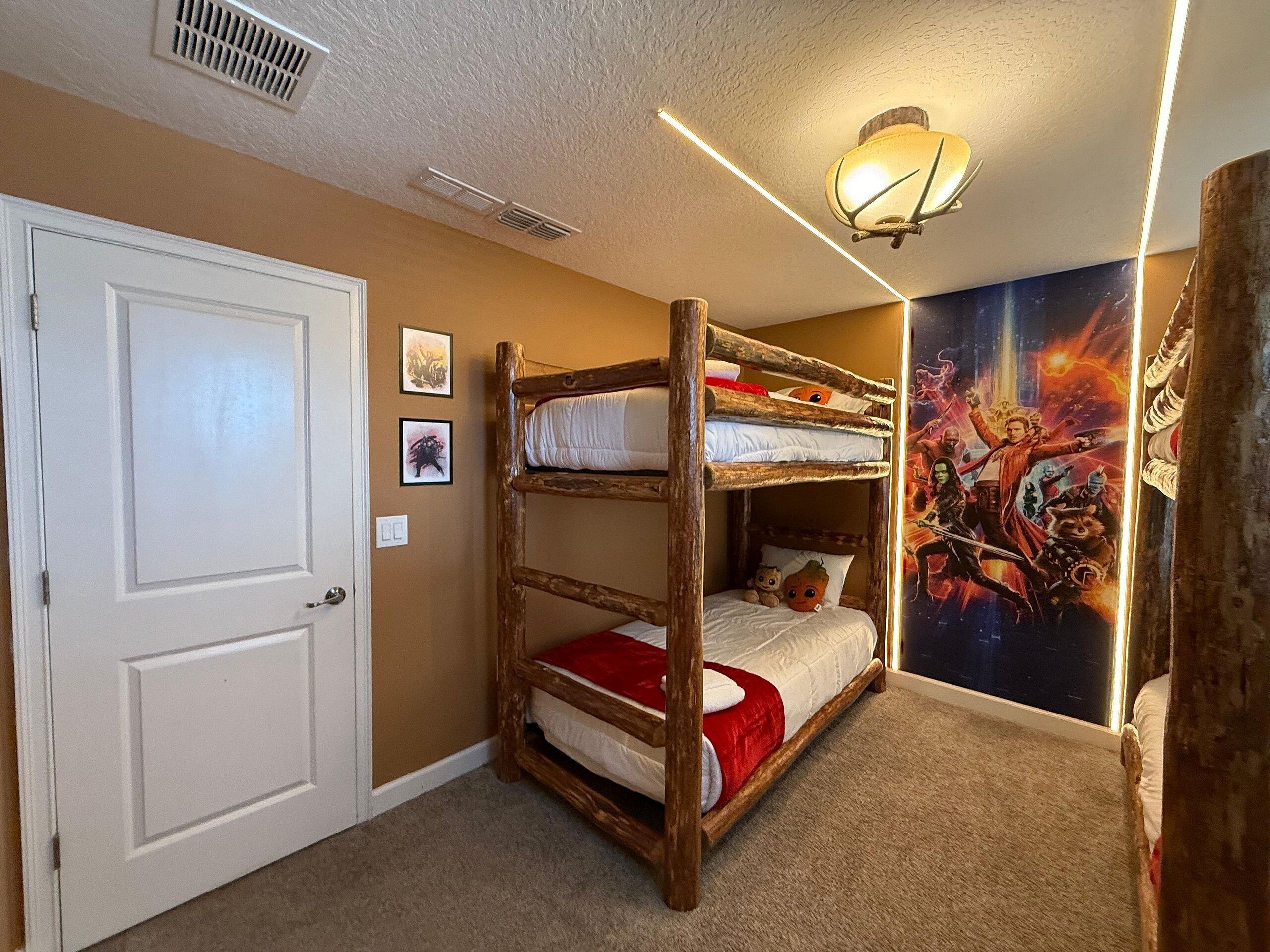 Une chambre avec un lit superposé, une porte, des bouches d’aération fixées au mur, un luminaire au plafond et une affiche accrochée au mur.