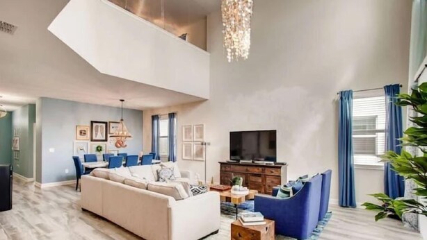 Un salon spacieux avec un plafond haut, un grand téléviseur et un coin repas avec des chaises bleues.