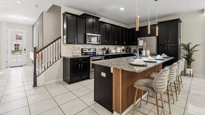 A modern kitchen with dark cabinets, a central island, and bar stools. - Special 5BR home at Solara Resort (Kissimmee)