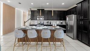 A modern kitchen with dark cabinets, stainless steel appliances, and a central island with bar stools. - Special 5BR home at Solara Resort (Kissimmee)