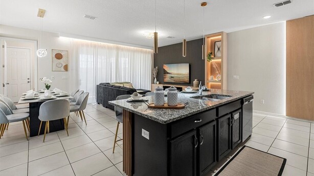 A modern kitchen with a central island, a dining area with a table and chairs, and a living area with a sofa and a TV. - Special 5BR home at Solara Resort (Kissimmee)