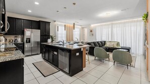 A modern kitchen with dark cabinets, a stainless steel refrigerator, and a central island with a sink. - Special 5BR home at Solara Resort (Kissimmee)