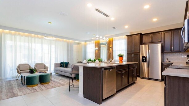 A modern kitchen with a central island, stainless steel appliances, and dark wooden cabinets. - Modern 6BR Home with Water Club House (Kissimmee)