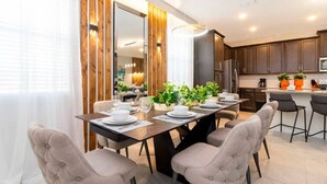A modern dining area with a wooden accent wall, a large mirror, and a kitchen in the background. - Modern 6BR Home with Water Club House (Kissimmee)