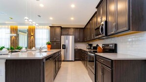 A modern kitchen with dark wood cabinets, stainless steel appliances, and a central island. - Modern 6BR Home with Water Club House (Kissimmee)