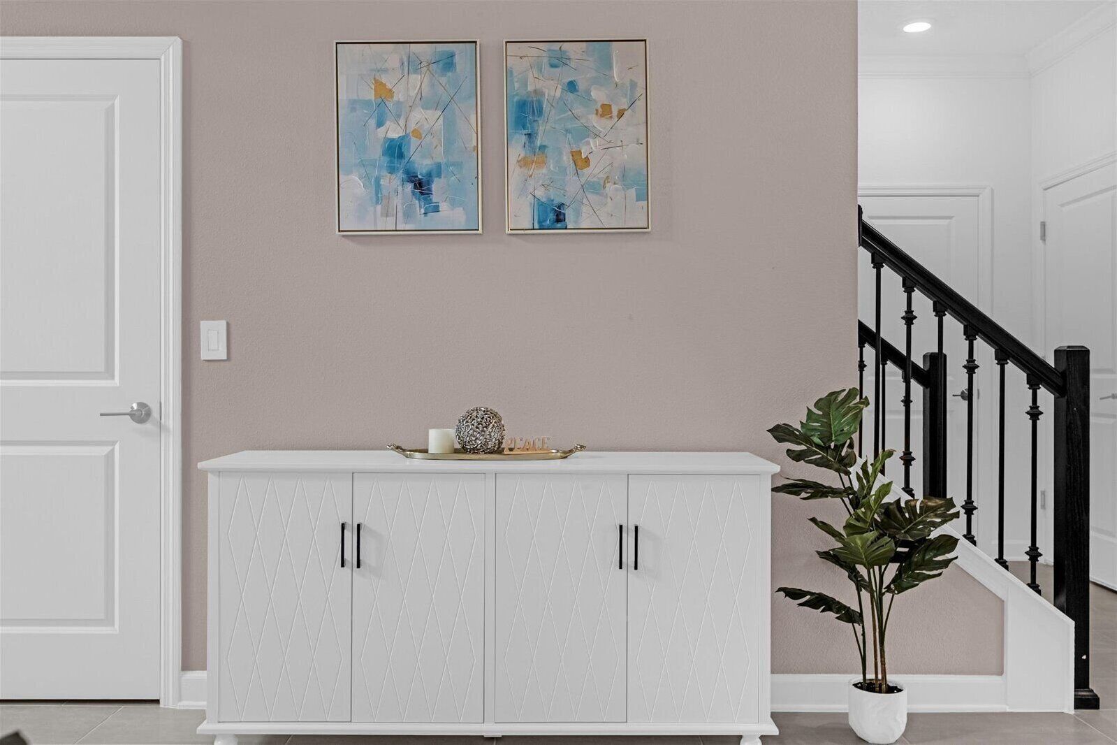Ein Flur mit einem weißen Schrank, zwei abstrakten Gemälden an der Wand und einer Treppe mit schwarzen Geländern.