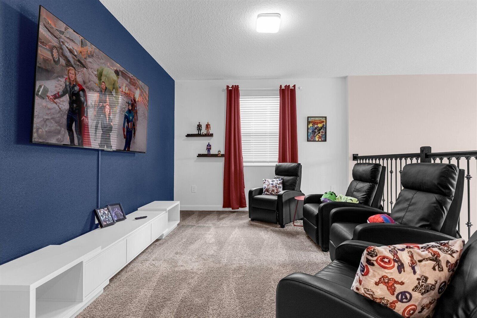 Una sala de estar con una pared azul decorativa, un televisor montado, un mueble blanco para entretenimiento, dos sillas de cuero negro, una cortina roja y una ventana con persianas.
